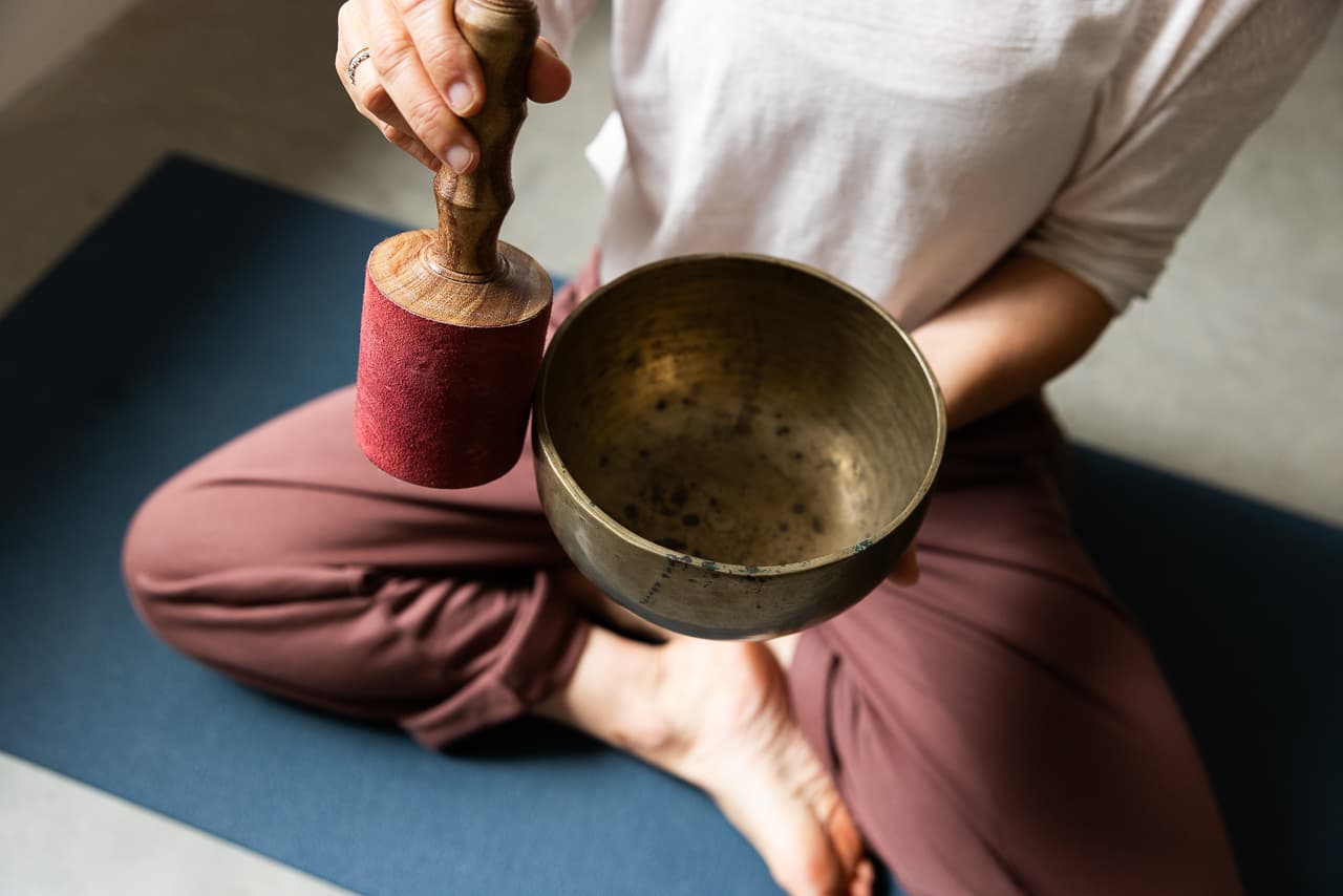 yogi gezeten in kleermnakerszit die een klankschaal aanslaat